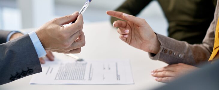 Close-up of couple signing contract with real estate agent in the office.