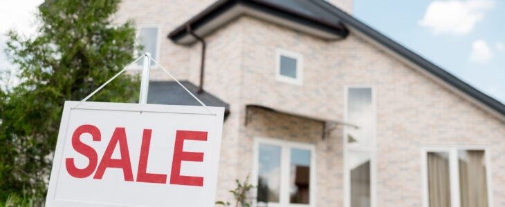 close up shot of wooden placard with sale sign in front of modern cottage