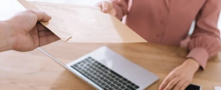 Courier handing envelope to person at desk with laptop.