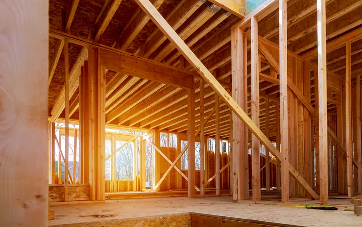 Wooden frame of a house under construction with sunlight streaming through.